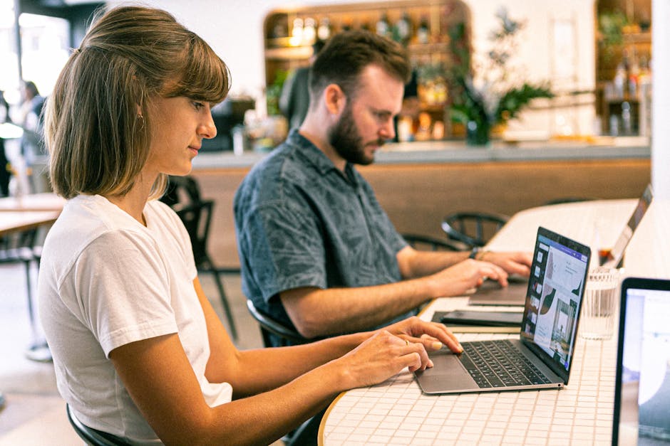 Two young professionals working on laptops in a modern cafe setting