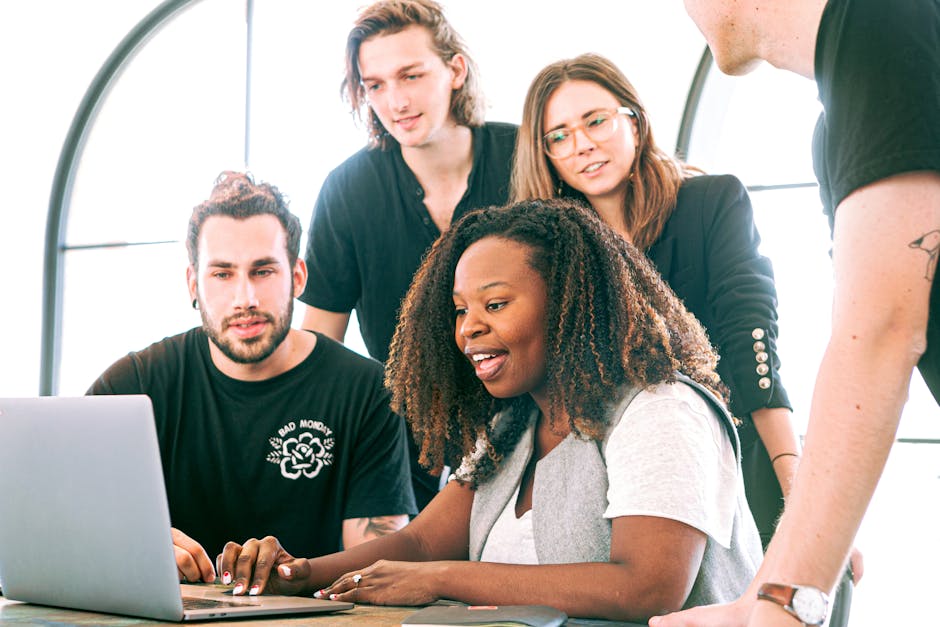 A diverse group of young professionals collaborating around a laptop in a modern office setting
