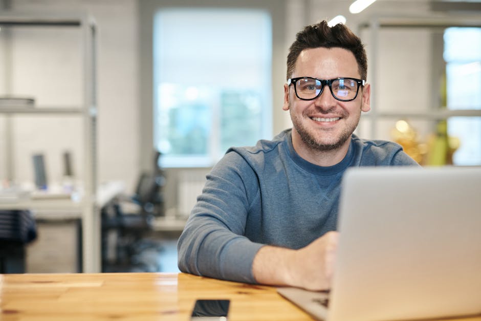 Happy man wearing glasses working remotely on laptop in modern office environment